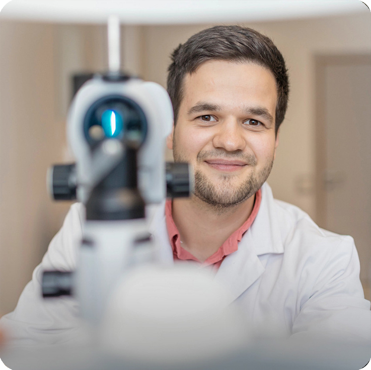 一名身穿白大褂的男子通过光学仪器的目镜专注地观察一个物体。